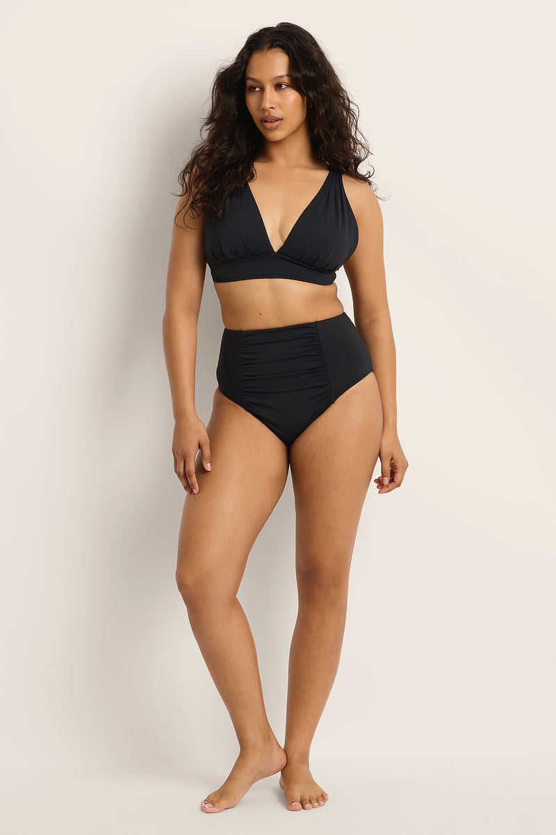 Woman wearing a Fearless supportive bust and high waist black bikini against a plain background.