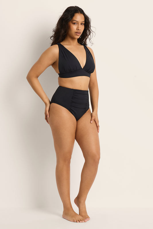 Woman wearing a Fearless supportive bust and high waist black bikini against a plain background.