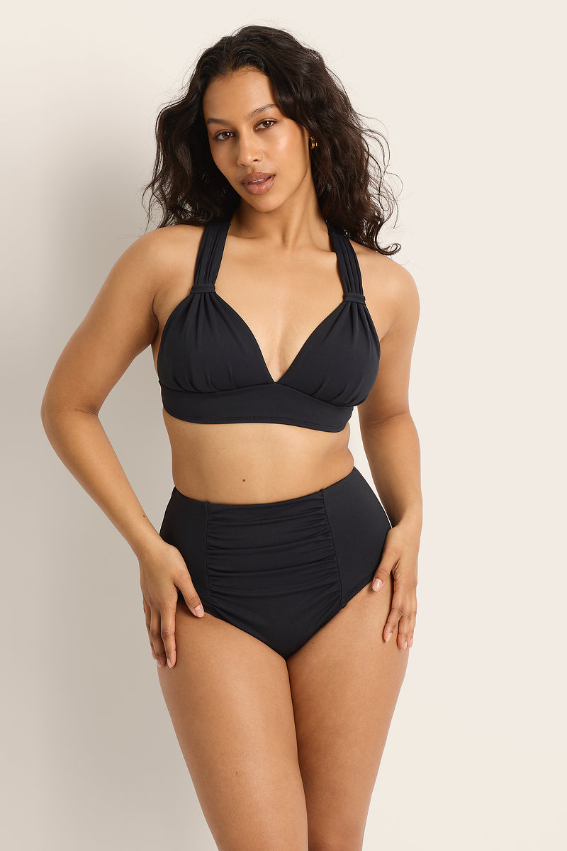 Woman wearing a Fearless supportive bust and high waist black bikini against a plain background.
