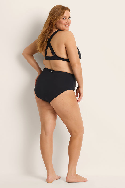 Woman wearing a Fearless supportive bust and high waist black bikini against a plain background.