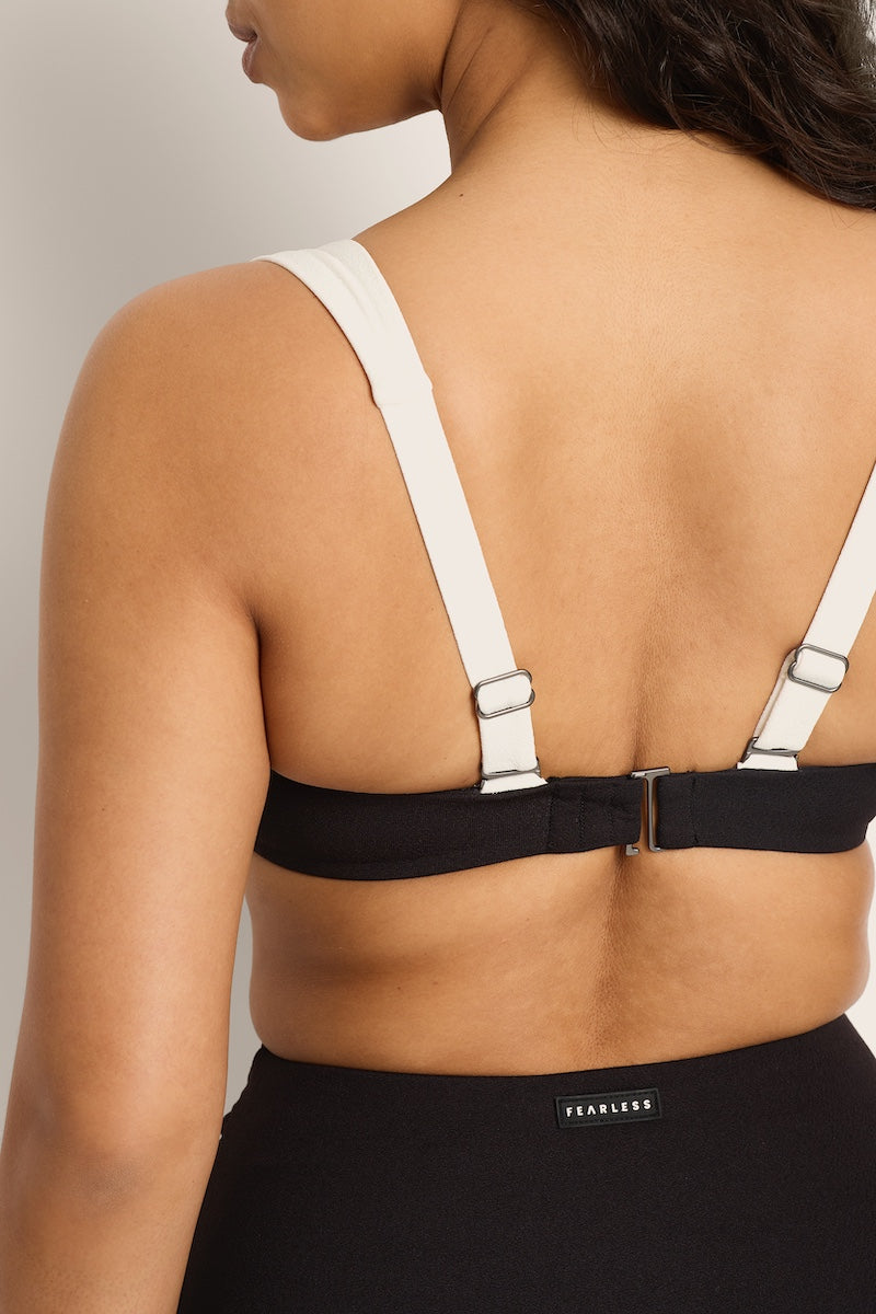 Black bra with white straps worn by a model on a neutral background