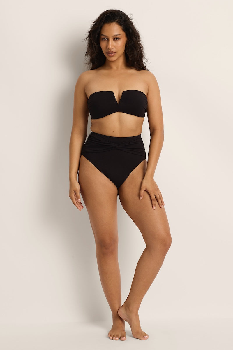 Woman wearing a black strapless top and high-waisted bikini bottom on a plain background