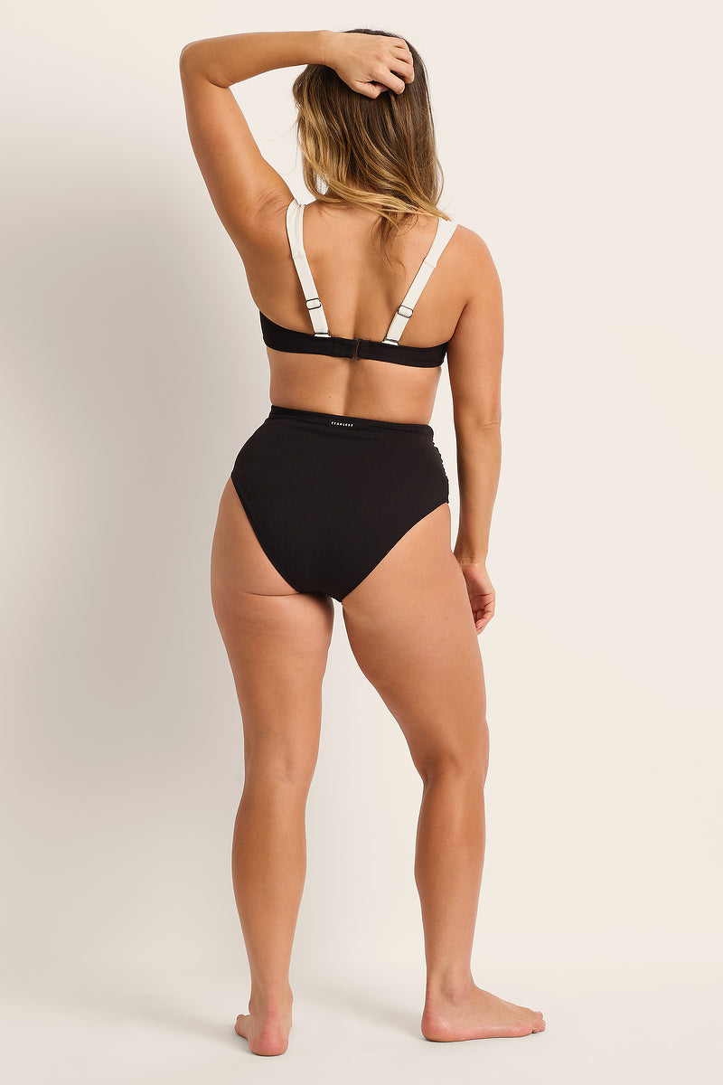 Woman wearing a black bikini with white straps on a plain background