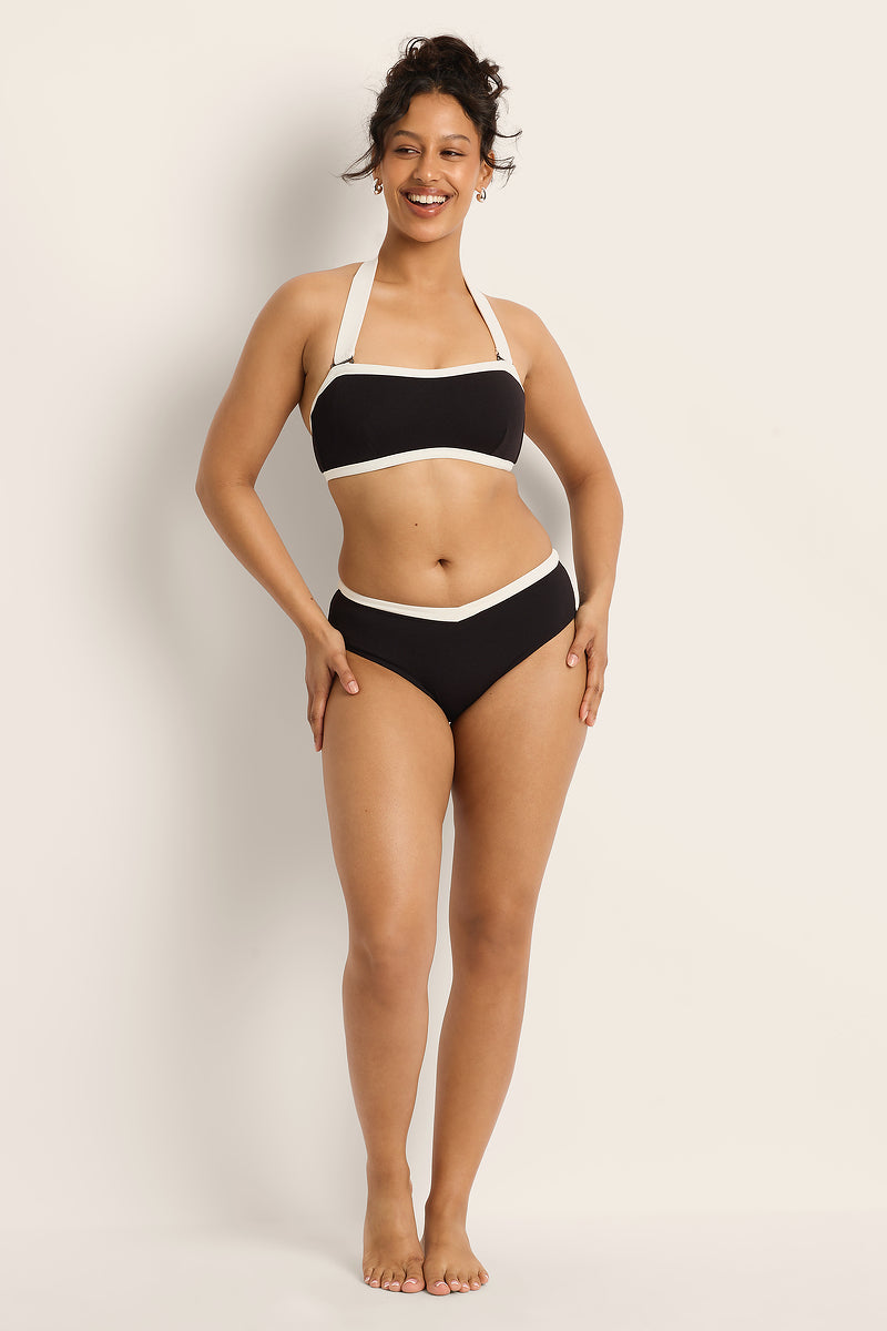 Woman wearing a black bikini with white straps against a plain background