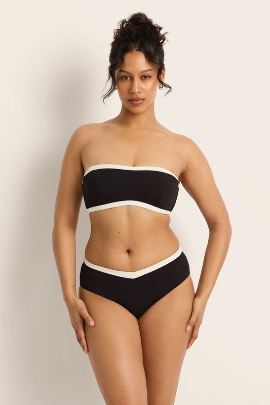 Woman wearing a black and white strapless bikini against a plain background