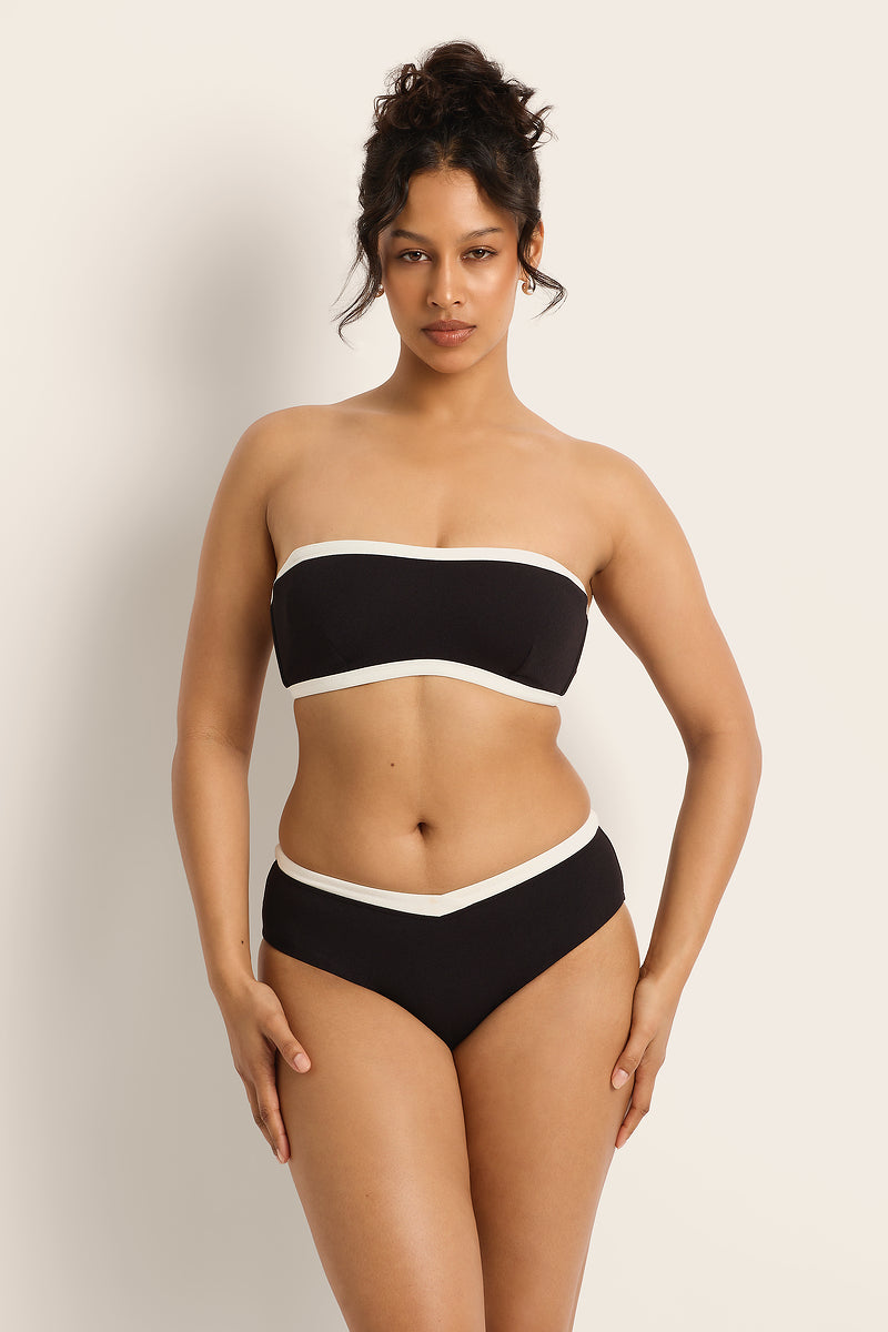 Woman wearing a black and white strapless bikini against a plain background