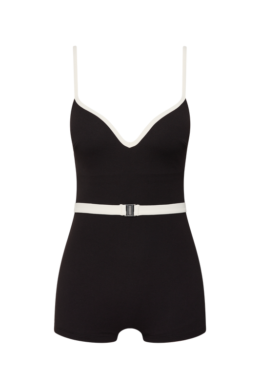 The Grace Boyleg by Fearless au is a matte black one-piece bodysuit made from recycled crinkle fabric, featuring white trim, thin white straps, a V-neckline, a white belt with black buckle, and a comfortable short boyleg cut.