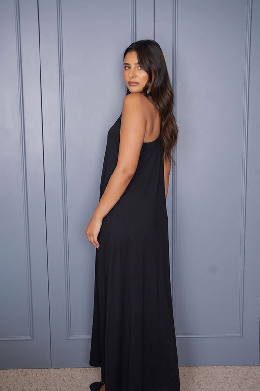A woman wearing a sleeveless black maxi dress, photographed from the back against a blue-gray paneled wall.