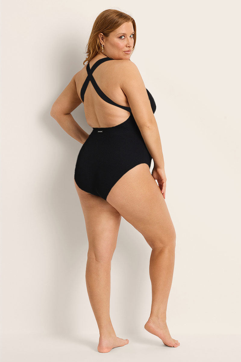 Woman wearing a black swimsuit with thin straps on a plain background