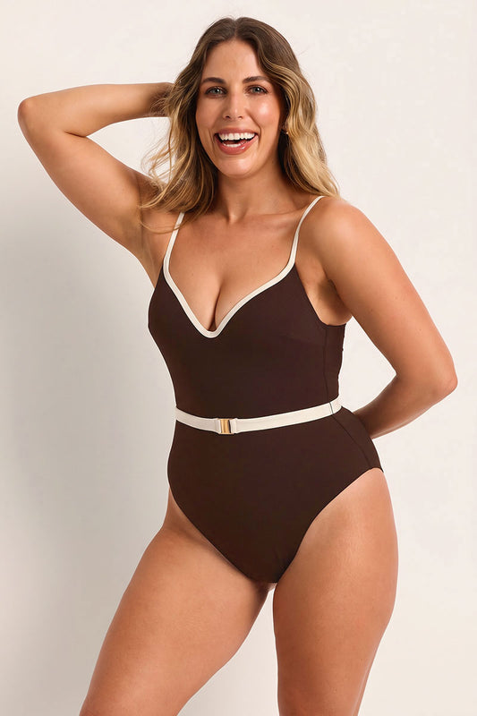 Woman wearing a brown swimsuit with white trim on a plain background